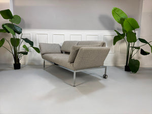 Fabrikverkauf Brühl Roro Designer Stoff Sofa vor einer Wand, stilvoll und modern eingerichtet.