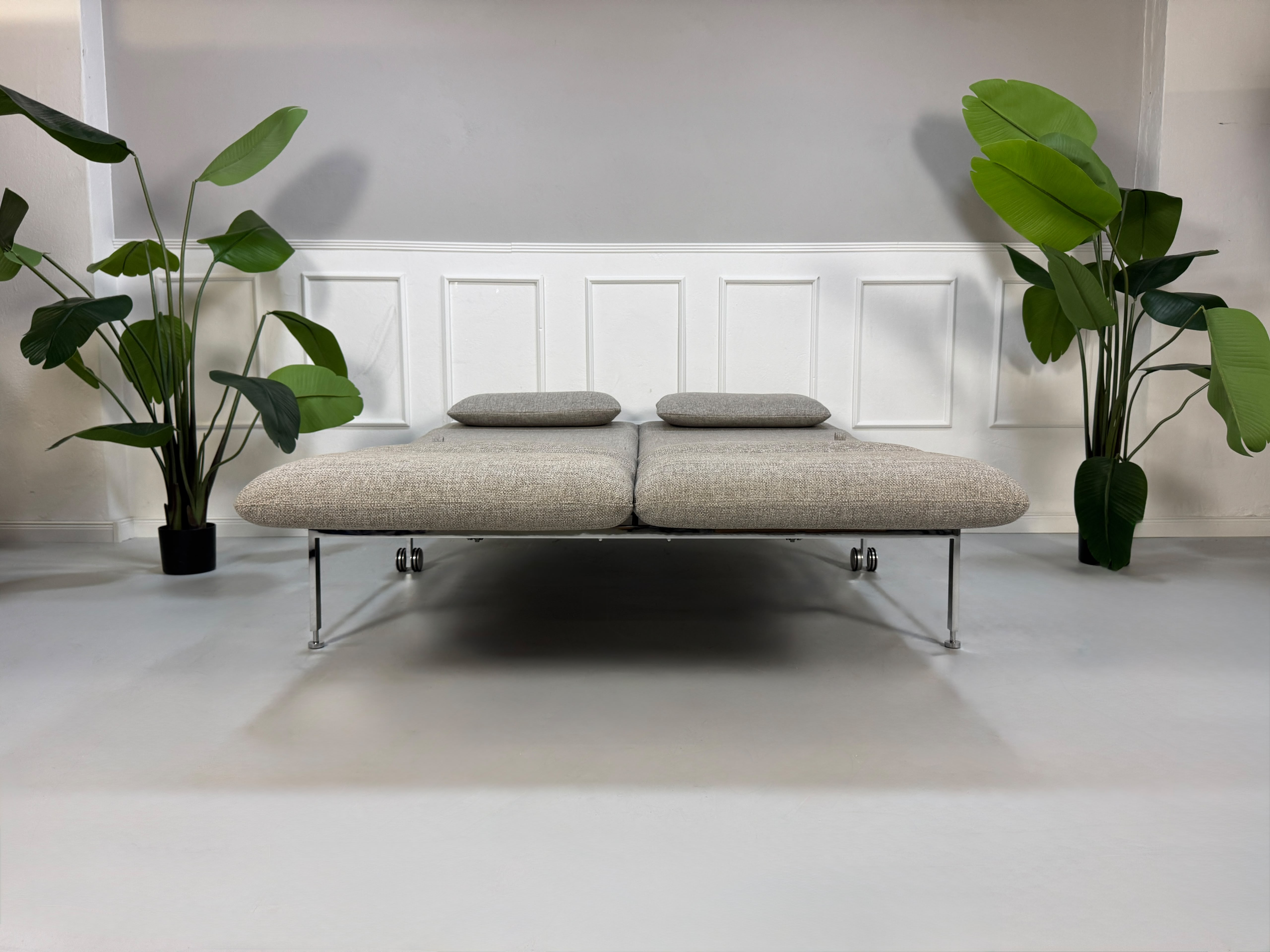 Fabrikverkauf Brühl Roro Designer Stoff Sofa vor einer Wand, stilvoll und modern eingerichtet.