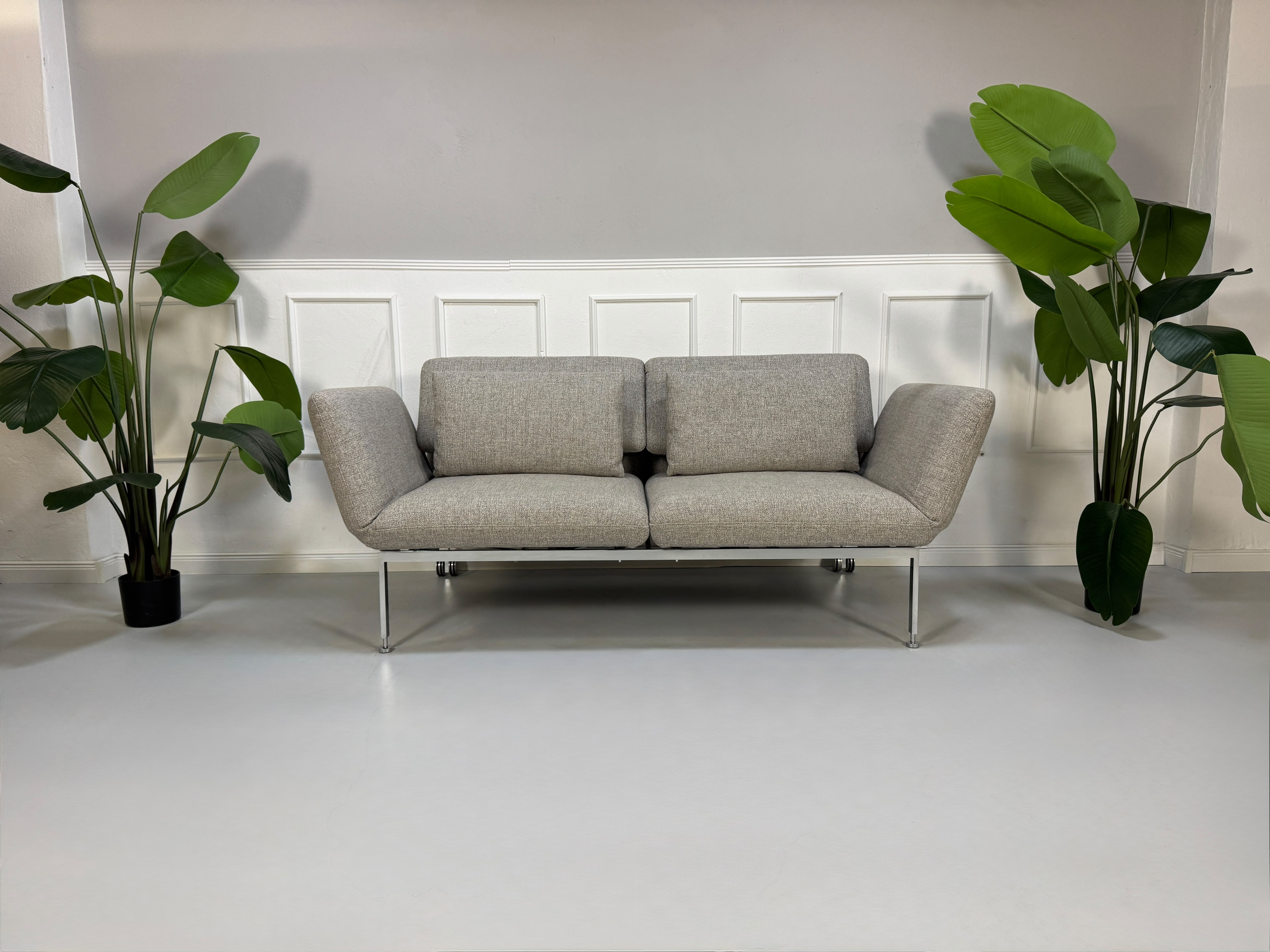Fabrikverkauf Brühl Roro Designer Stoff Sofa vor einer Wand, stilvoll und modern eingerichtet.
