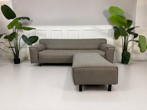 Gebrauchtes graues Rolf Benz Grata Designer Stoff Sofa mit Hocker vor einer Wand, stilvoll und modern eingerichtet.