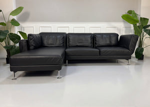 Gebrauchtes schwarzes Brühl Moule Designer Leder Sofa vor einer Wand, stilvoll und modern eingerichtet.