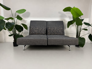 Gebrauchtes graues Brühl Moule Designer Stoff Sofa vor einer Wand, stilvoll und modern eingerichtet.