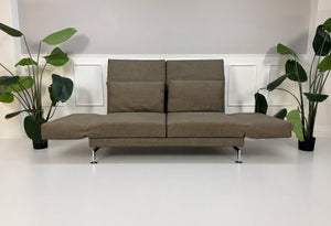Gebrauchtes braunes Brühl Moule Designer Stoff Sofa vor einer Wand, stilvoll und modern eingerichtet.