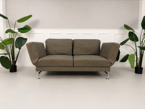 Gebrauchtes braunes Brühl Moule Designer Stoff Sofa vor einer Wand, stilvoll und modern eingerichtet.