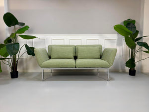 Fabrikverkauf grünes Brühl Roro Designer Stoff Sofa vor einer Wand, stilvoll und modern eingerichtet.