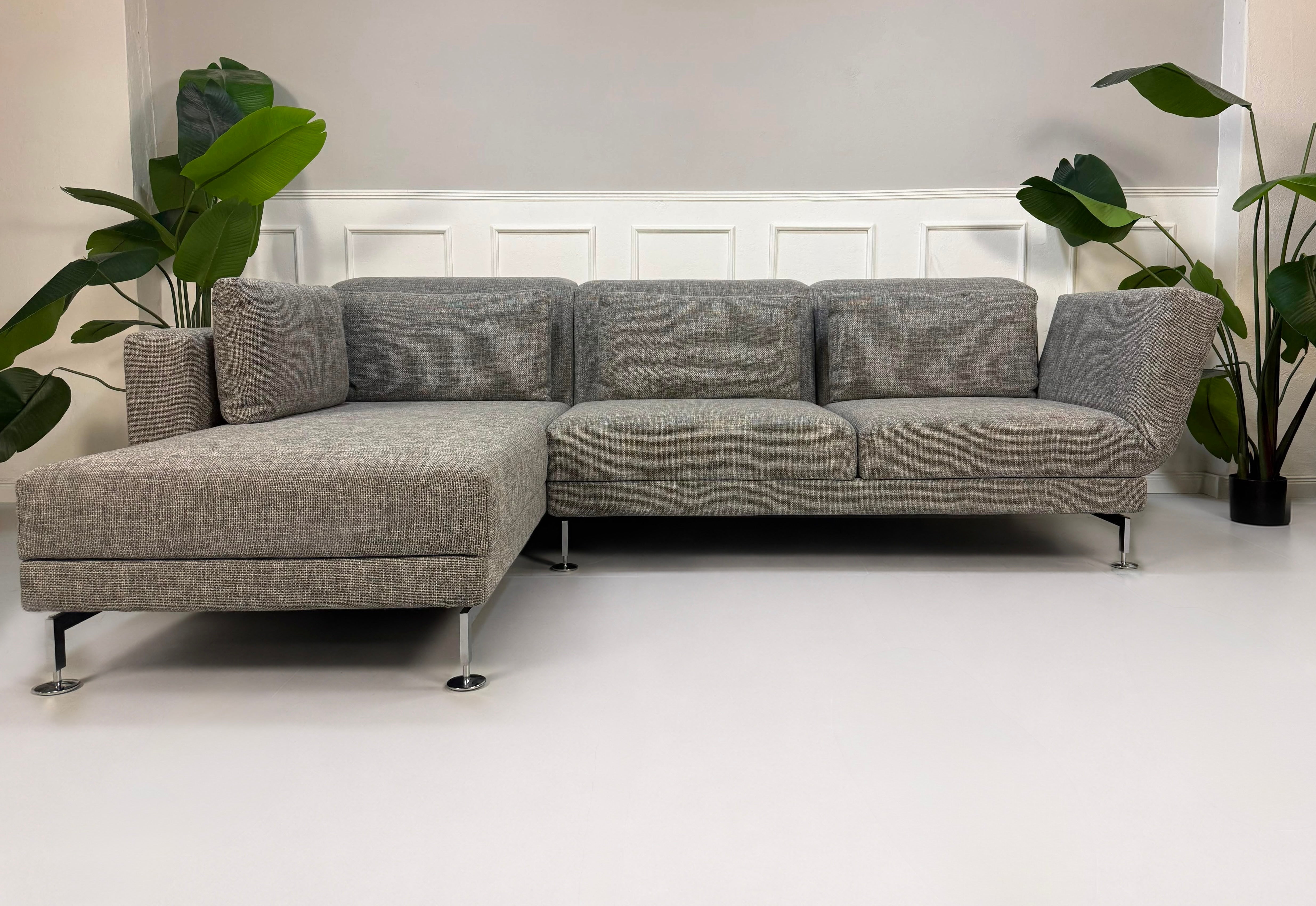 Gebrauchtes graues Brühl Designer Stoff Sofa vor einer Wand, stilvoll und modern eingerichtet.