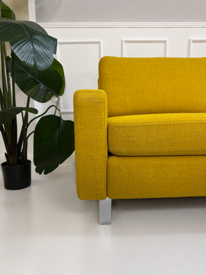 Gelbes Ausstellungsstück COR Conseta Designer Stoff Sofa vor einer Wand, stilvoll und modern eingerichtet.