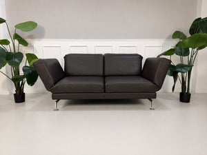 Gebrauchtes braunes Brühl Moule Designer Leder Sofa vor einer Wand, stilvoll und modern eingerichtet.