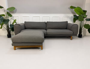 Gebrauchtes graues Muuto Rest Designer Stoff Sofa mit Hocker vor einer Wand, stilvoll und modern eingerichtet.