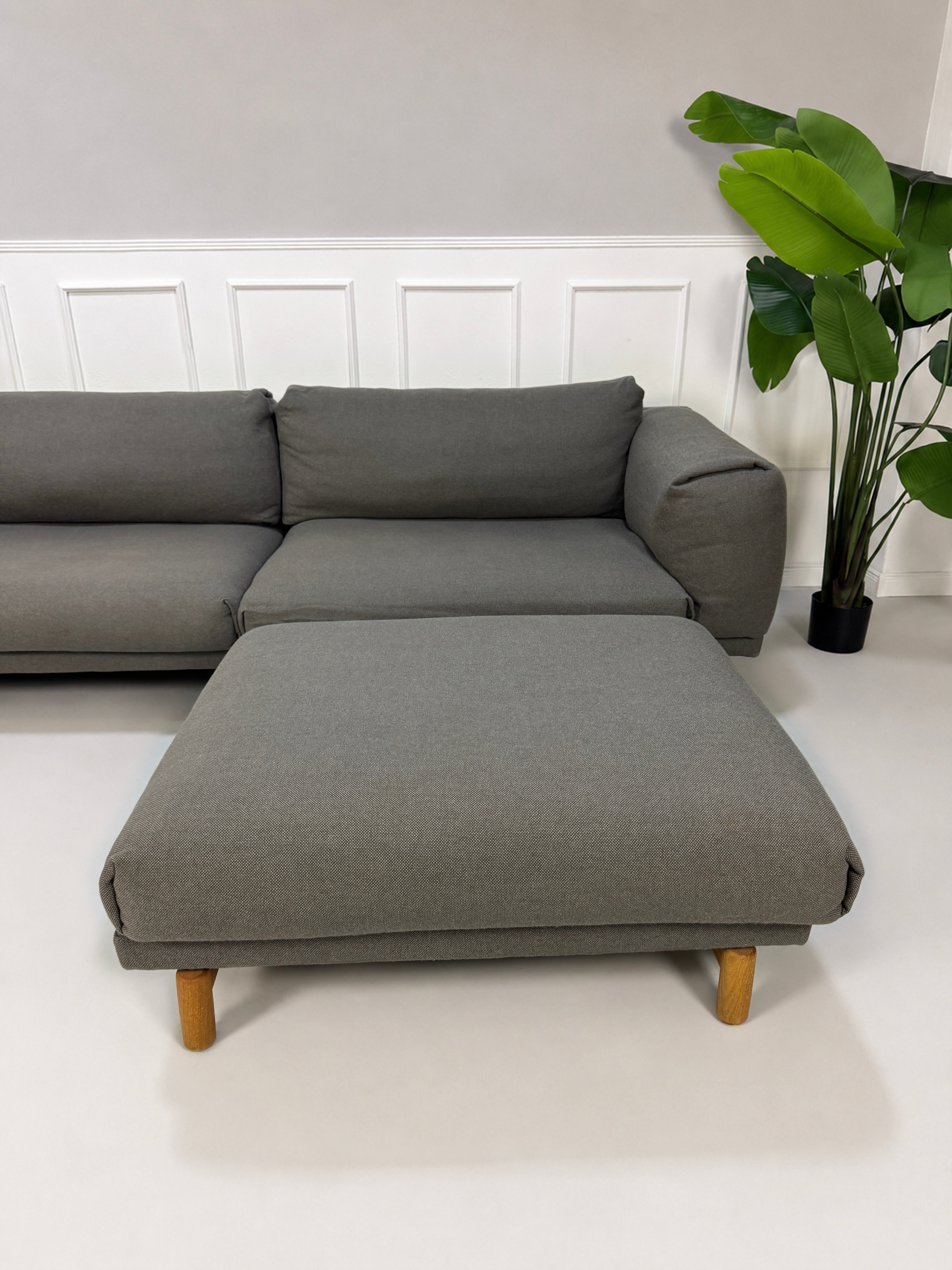 Gebrauchtes graues Muuto Rest Designer Stoff Sofa mit Hocker vor einer Wand, stilvoll und modern eingerichtet.