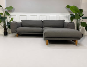 Gebrauchtes graues Muuto Rest Designer Stoff Sofa mit Hocker vor einer Wand, stilvoll und modern eingerichtet.