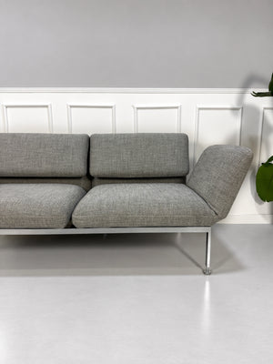 Gebrauchtes graues Brühl Roro Medium Designer Stoff Sofa vor einer Wand, stilvoll und modern eingerichtet.