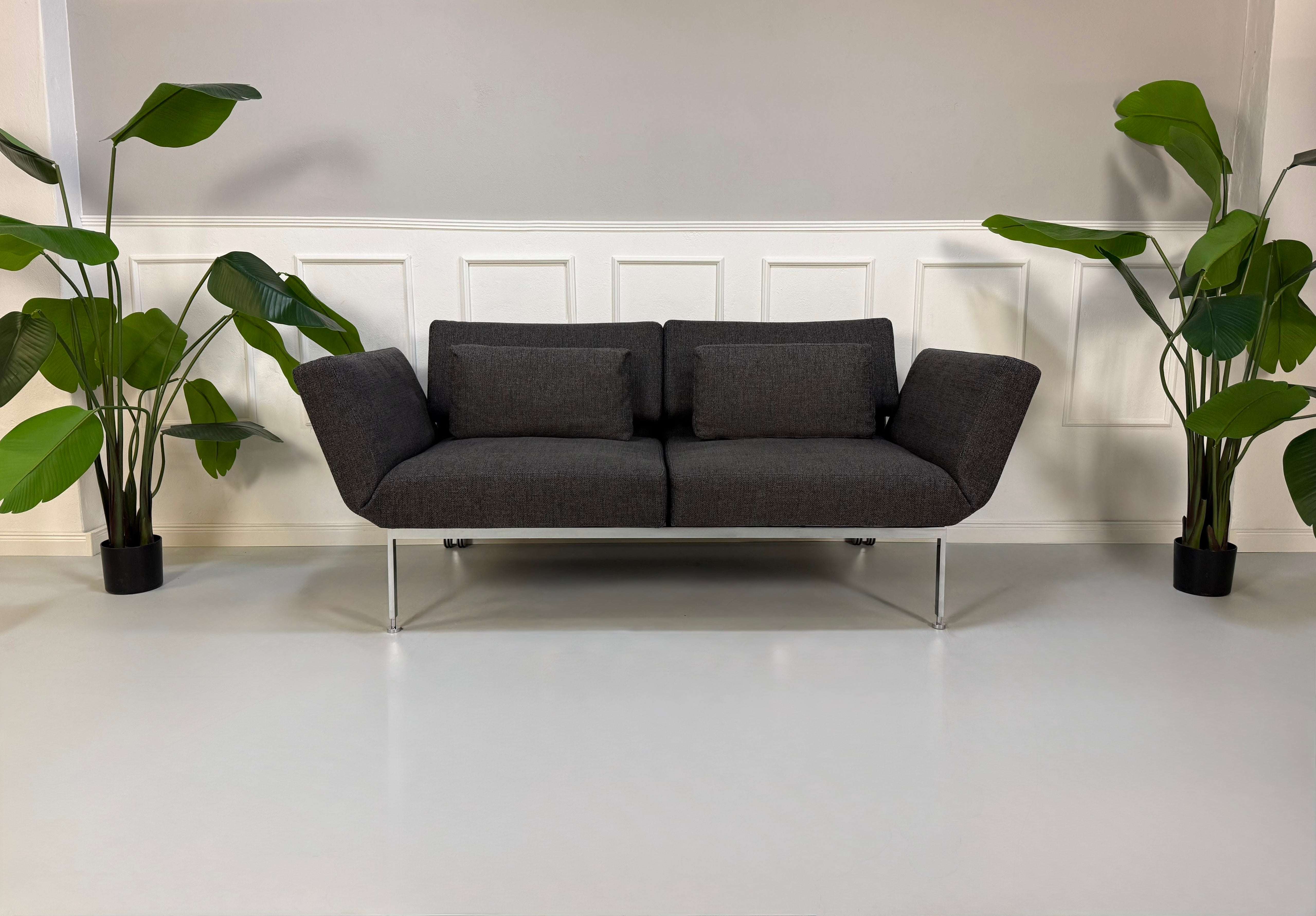 Gebrauchtes graues Brühl Roro Soft Designer Stoff Sofa vor einer Wand, stilvoll und modern eingerichtet.
