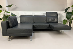 Gebrauchtes Grau Grün Brühl Moule Designer Leder Sofa vor einer Wand, stilvoll und modern eingerichtet.