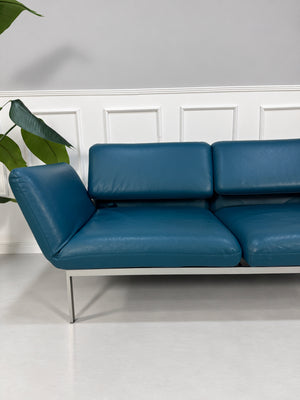 Gebrauchtes blaues Brühl Roro Medium Designer Leder Sofa vor einer Wand, stilvoll und modern eingerichtet.