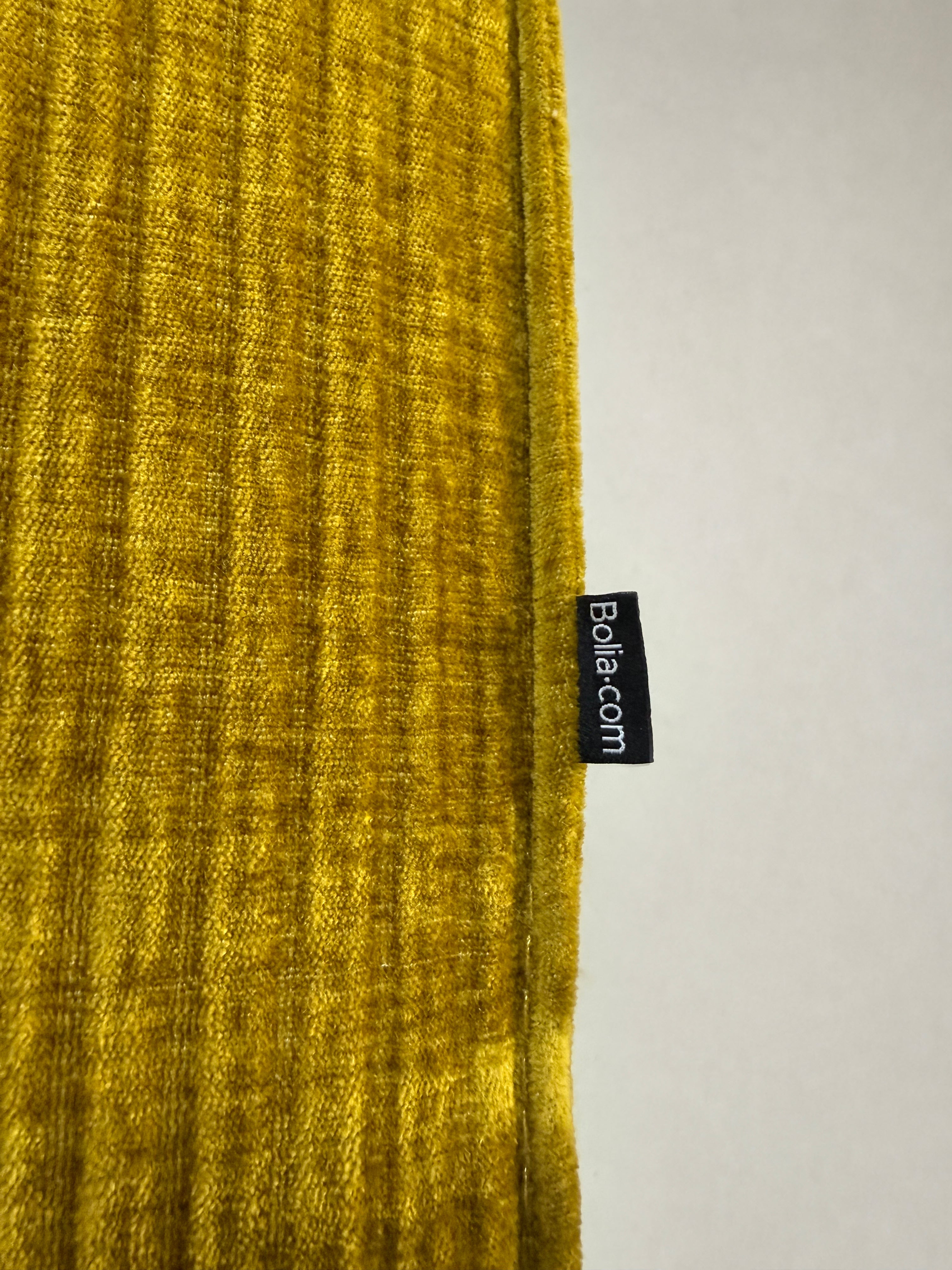Gebrauchte gelbe Bolia Cosima Designer Cord Hocker vor einer Wand, stilvoll und modern eingerichtet.
