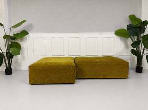 Gebrauchte gelbe Bolia Cosima Designer Cord Hocker vor einer Wand, stilvoll und modern eingerichtet.