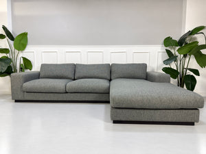 Gebrauchtes graues Bolia Sepia Designer Stoff Ecksofa vor einer Wand, stilvoll und modern eingerichtet.