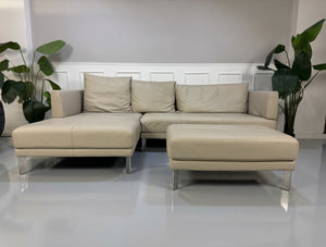 Gebrauchtes beiges Rolf Benz Sento 344 Designer Leder Ecksofa mit Hockerbank vor einer Wand, stilvoll und modern eingerichtet.