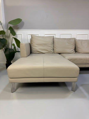 Gebrauchtes beiges Rolf Benz Sento 344 Designer Leder Ecksofa mit Hockerbank vor einer Wand, stilvoll und modern eingerichtet.