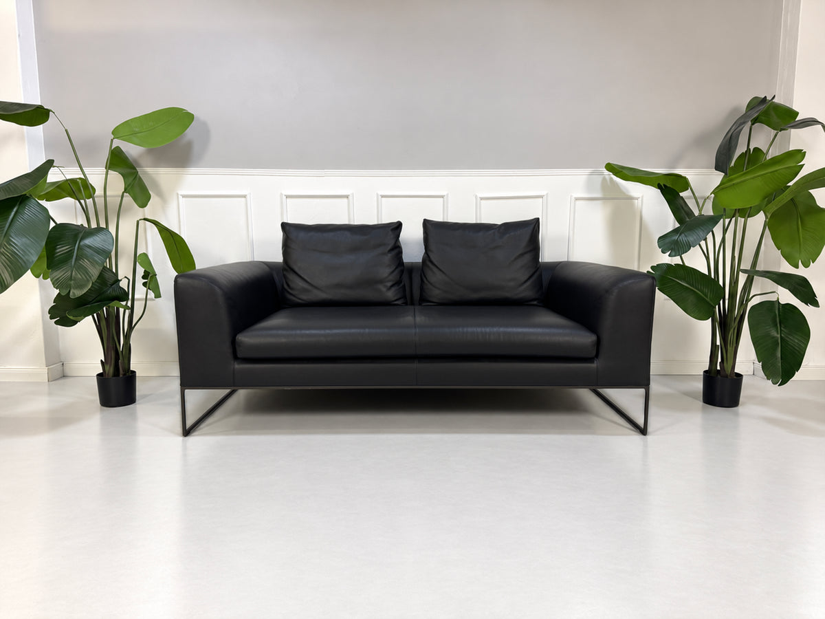 Gebrauchtes schwarzes COR Mell Designer Leder Sofa vor einer Wand, stilvoll und modern eingerichtet.