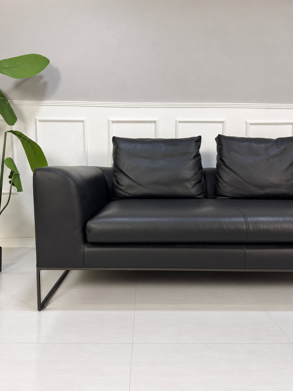 Gebrauchtes schwarzes COR Mell Designer Leder Sofa vor einer Wand, stilvoll und modern eingerichtet.
