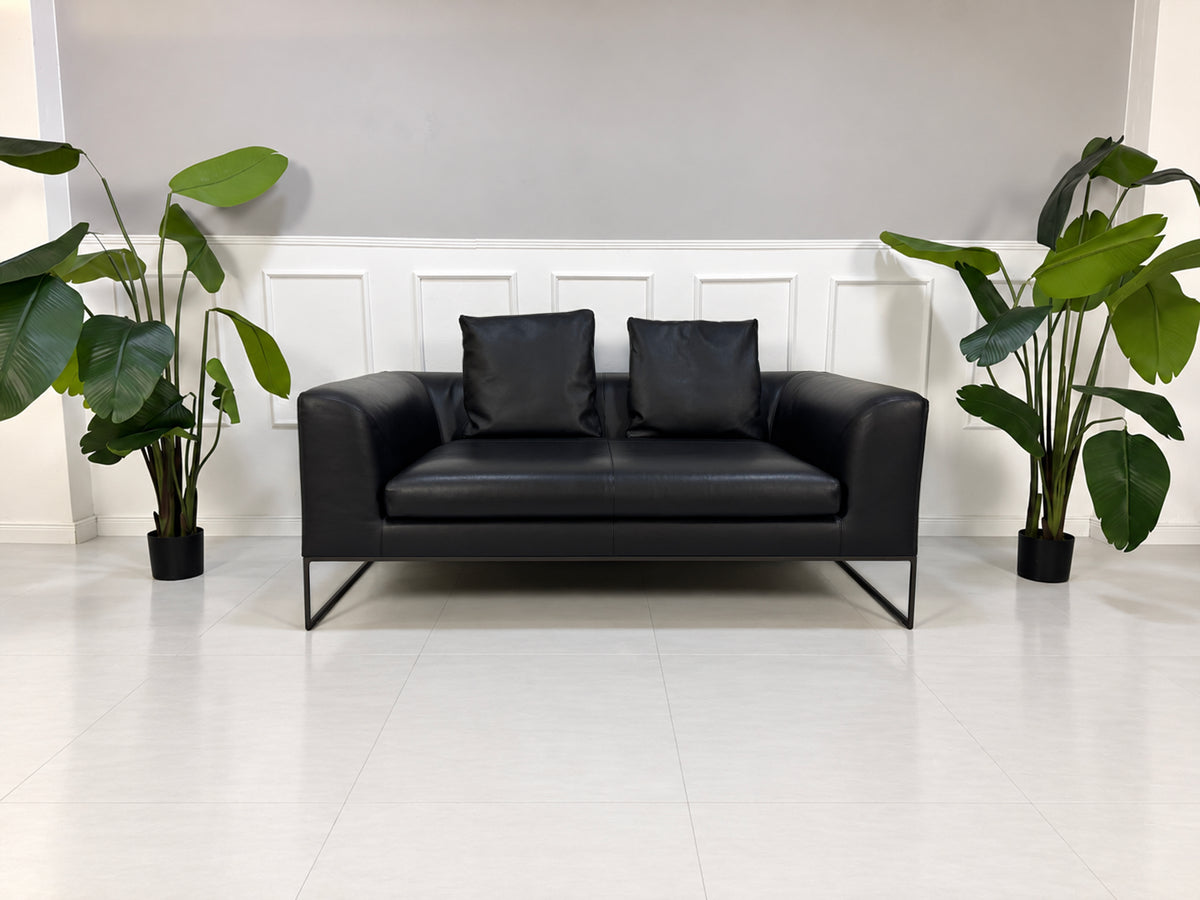 Gebrauchtes schwarzes COR Mell Designer Leder Sofa vor einer Wand, stilvoll und modern eingerichtet.