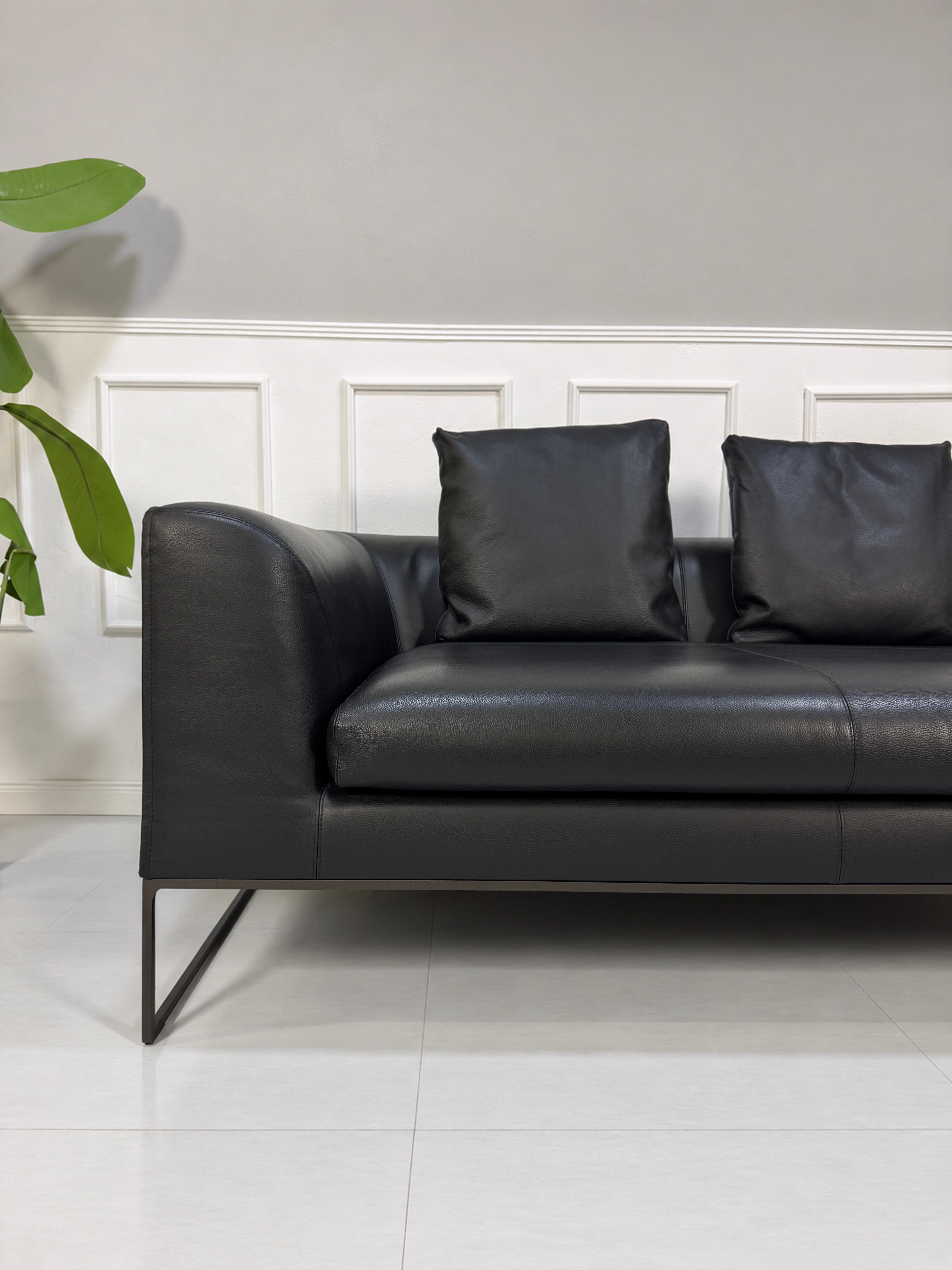 Gebrauchtes schwarzes COR Mell Designer Leder Sofa vor einer Wand, stilvoll und modern eingerichtet.