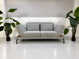 Gebrauchtes graues Brühl Moule Medium Designer Stoff Sofa mit Ablage und Hocker vor einer Wand, stilvoll und modern eingerichtet.