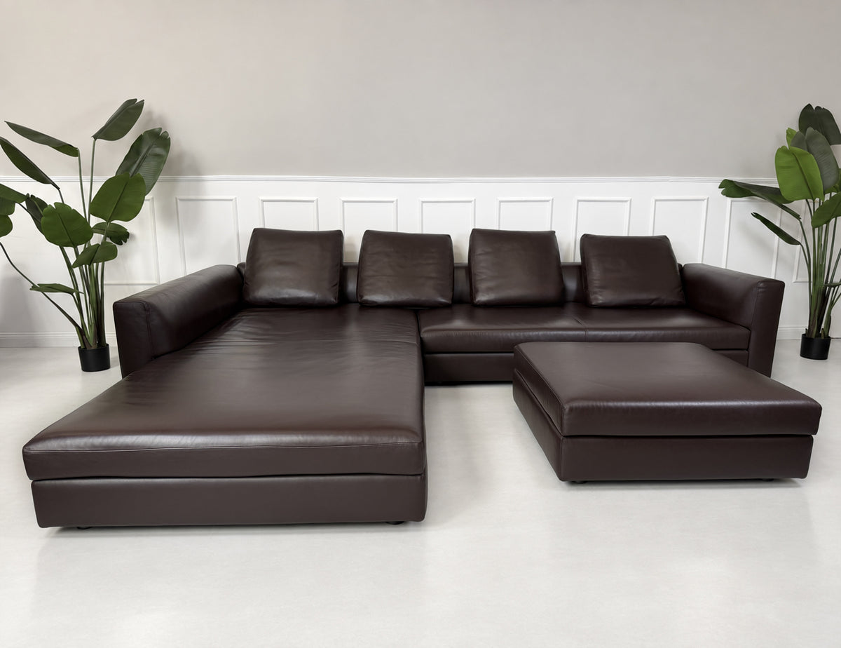 Gebrauchtes braunes Minotti Kline Designer Leder Ecksofa mit Hocker vor einer Wand, stilvoll und modern eingerichtet.