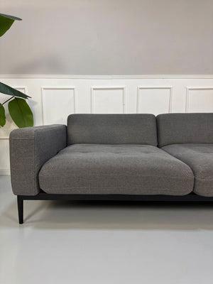Gebrauchtes graues Rolf Benz Tira Designer Stoff Sofa vor einer Wand, stilvoll und modern eingerichtet.