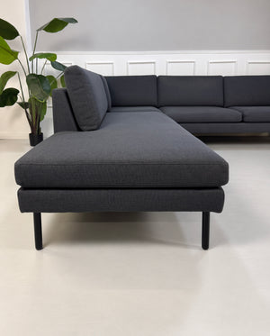 Gebrauchtes blaues Bolia Scandinavia Remix Designer Stoff Ecksofa vor einer Wand, stilvoll und modern eingerichtet.
