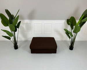 Gebrauchter brauner BoConcept Stoff Hocker vor einer Wand, stilvoll und modern eingerichtet.