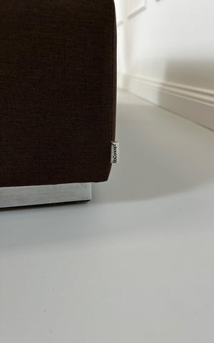 Gebrauchter brauner BoConcept Stoff Hocker vor einer Wand, stilvoll und modern eingerichtet.