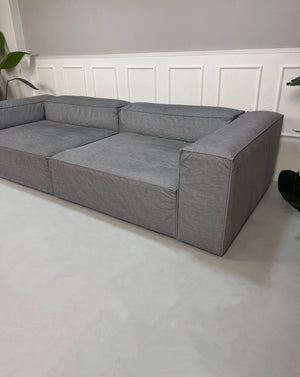 Gebrauchtes graues Bolia Cosima Designer Stoff Sofa vor einer Wand, stilvoll und modern eingerichtet.