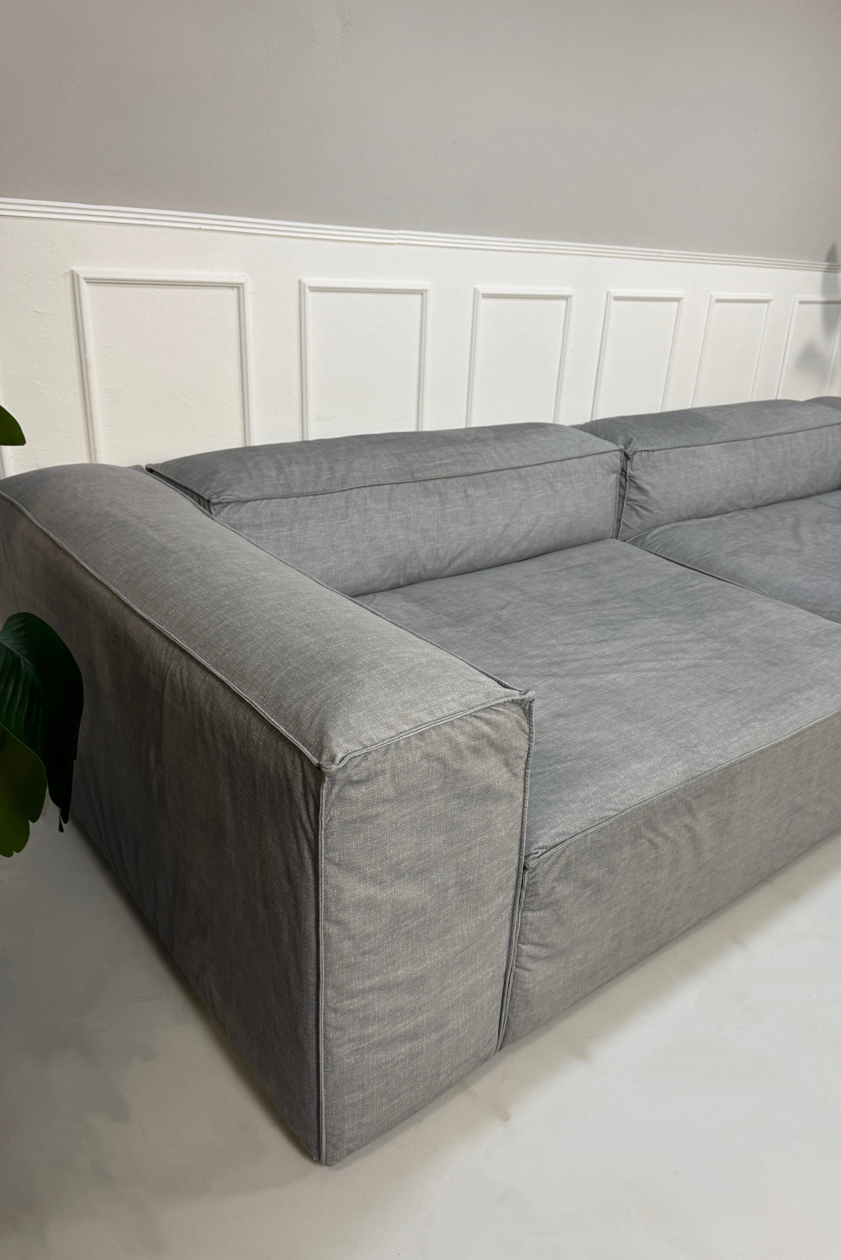 Gebrauchtes graues Bolia Cosima Designer Stoff Sofa vor einer Wand, stilvoll und modern eingerichtet.