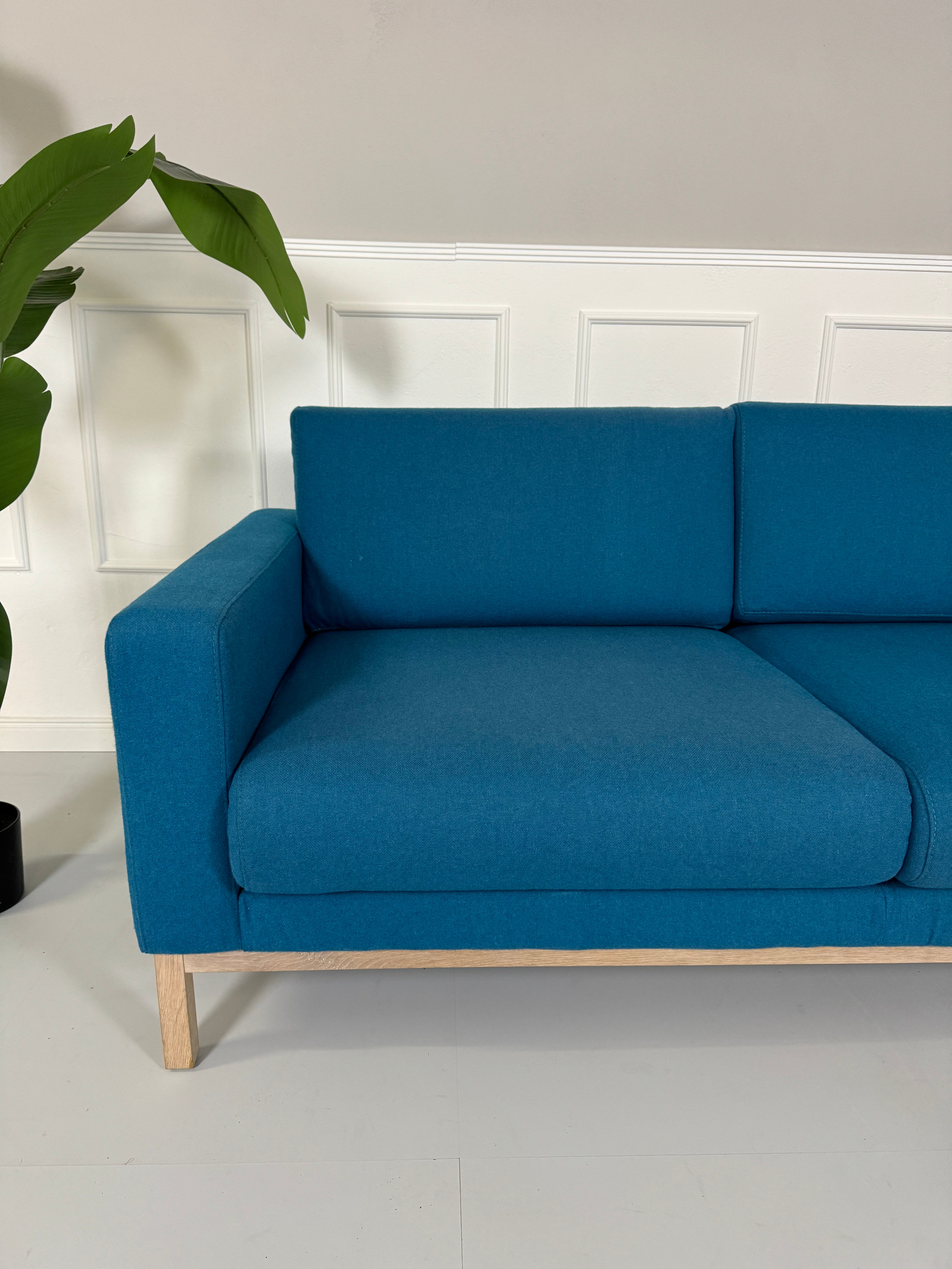 Gebrauchtes blaues petrol Bolia North Designer Stoff Sofa vor einer Wand, stilvoll und modern eingerichtet.