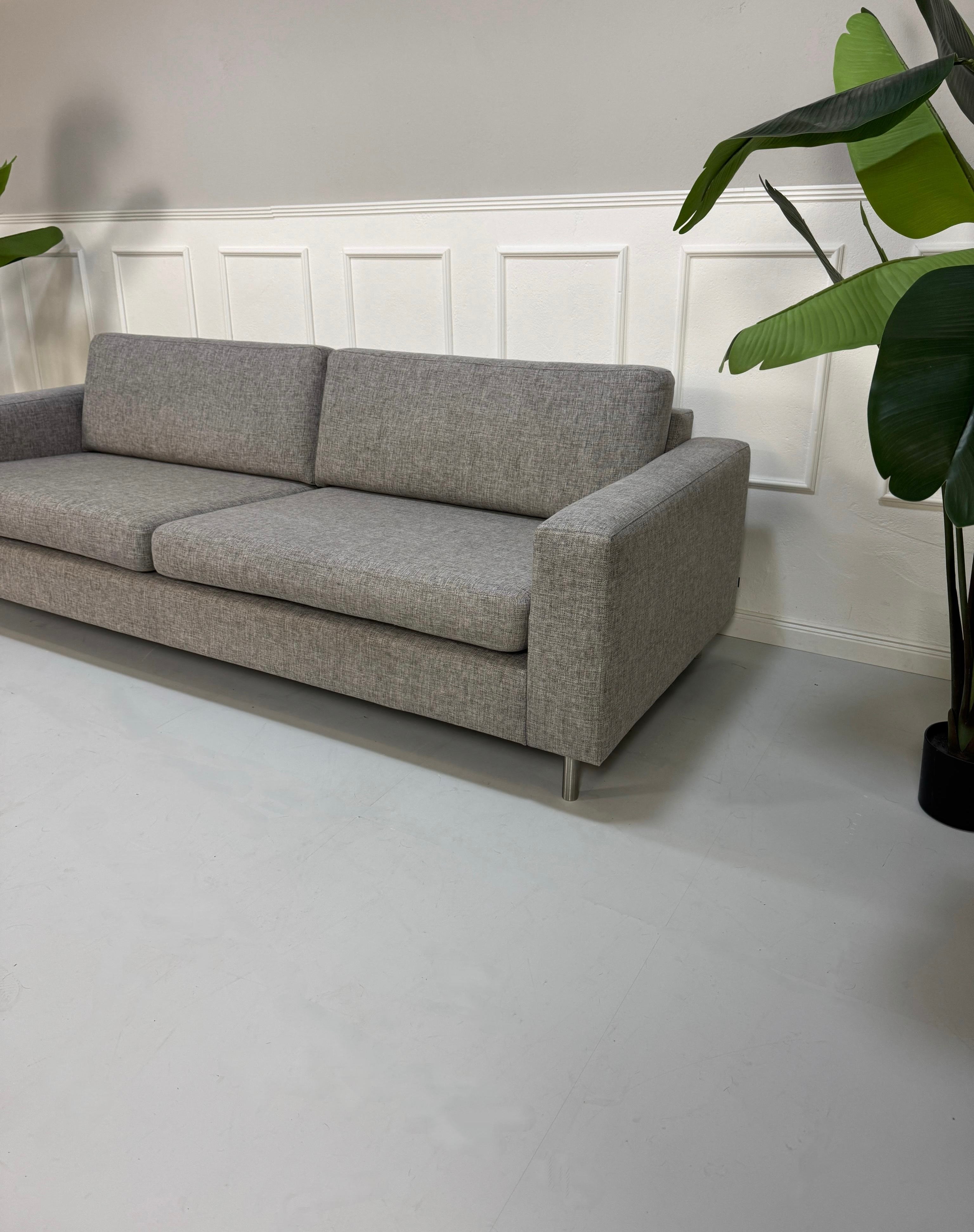 Gebrauchtes graues Bolia Scandinavia Designer Stoff Sofa mit Metallfüßen vor einer Wand, stilvoll und modern eingerichtet.
