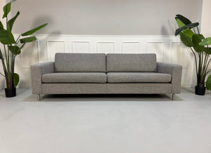 Gebrauchtes graues Bolia Scandinavia Designer Stoff Sofa mit Metallfüßen vor einer Wand, stilvoll und modern eingerichtet.