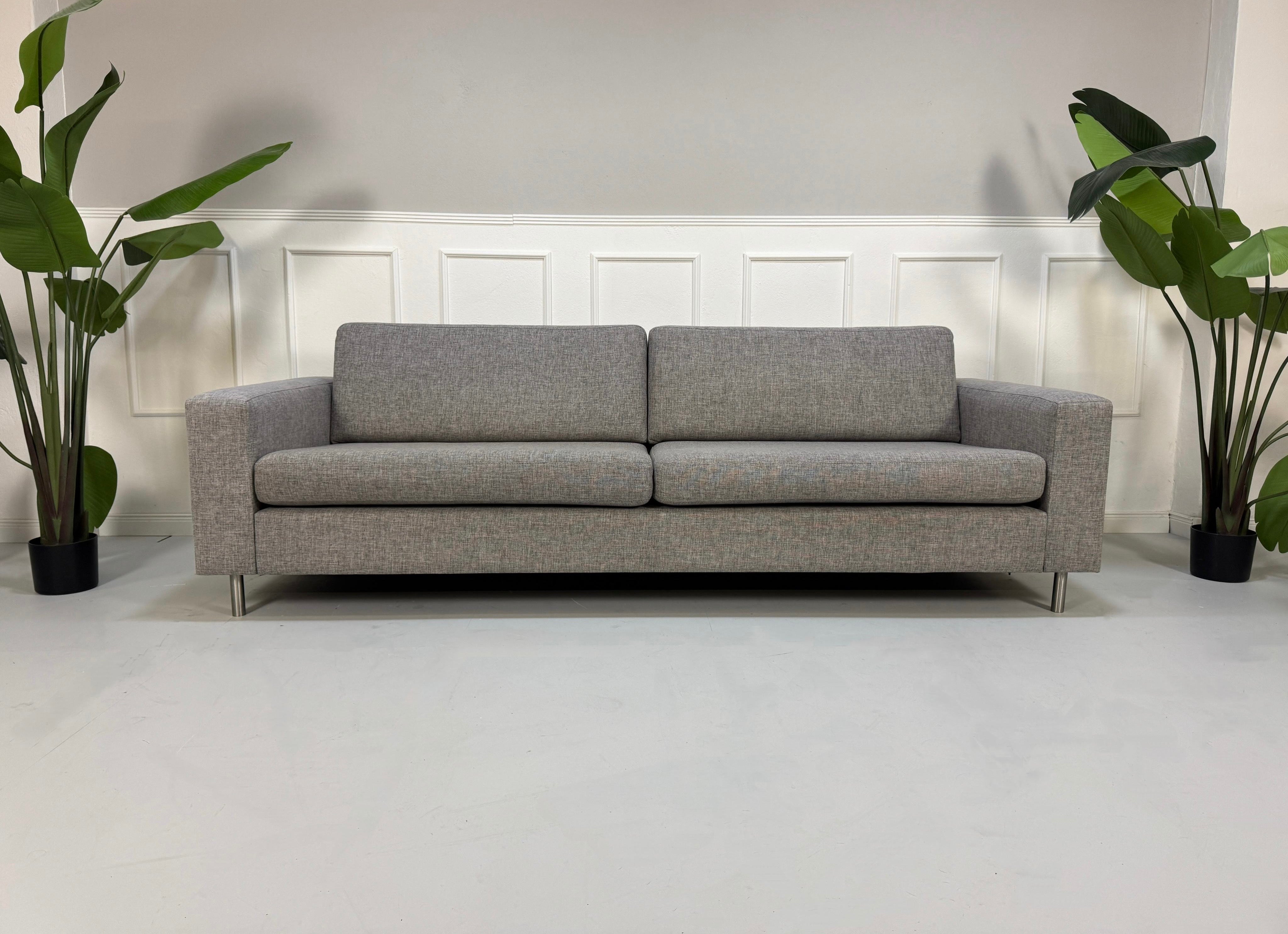 Gebrauchtes graues Bolia Scandinavia Designer Stoff Sofa mit Metallfüßen vor einer Wand, stilvoll und modern eingerichtet.