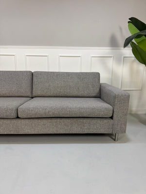 Gebrauchtes graues Bolia Scandinavia Designer Stoff Sofa mit Metallfüßen vor einer Wand, stilvoll und modern eingerichtet.
