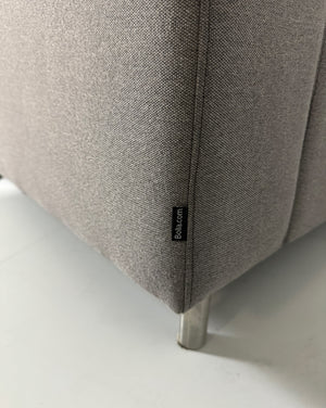 Gebrauchtes graues Bolia Scandinavia Stoff Sofa vor einer Wand, stilvoll und modern eingerichtet.