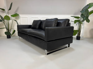 Gebrauchtes schwarzes Ledersofa Brühl Modell Alba vor einer modernen Wand