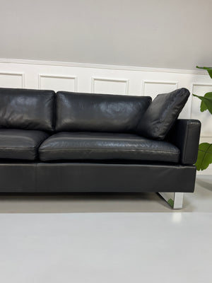 Gebrauchtes schwarzes Ledersofa Brühl Modell Alba vor einer modernen Wand