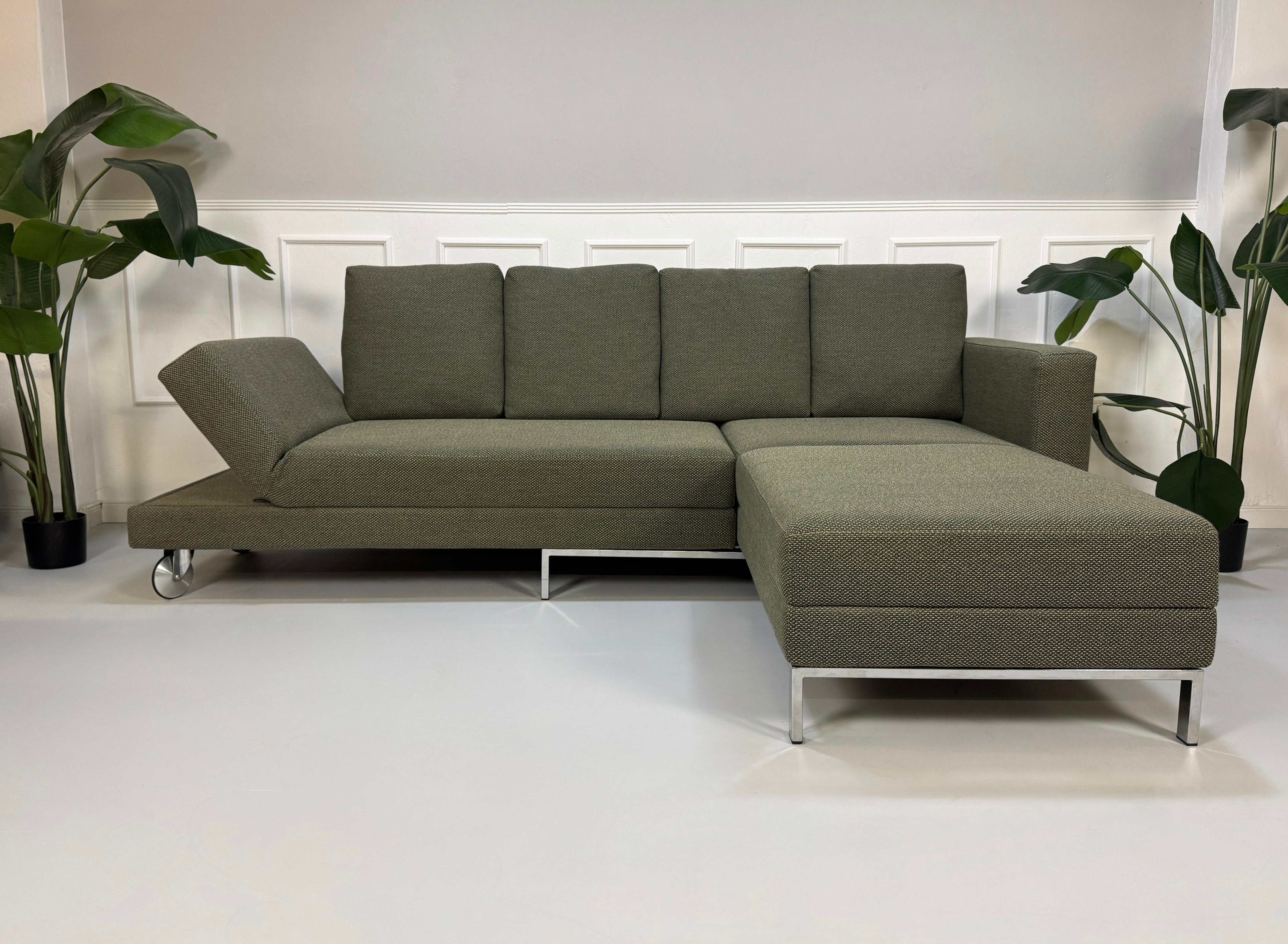 Grau Grünes Brühl Fourtwo Designer Stoff Sofa vor einer Wand, stilvoll und modern eingerichtet.