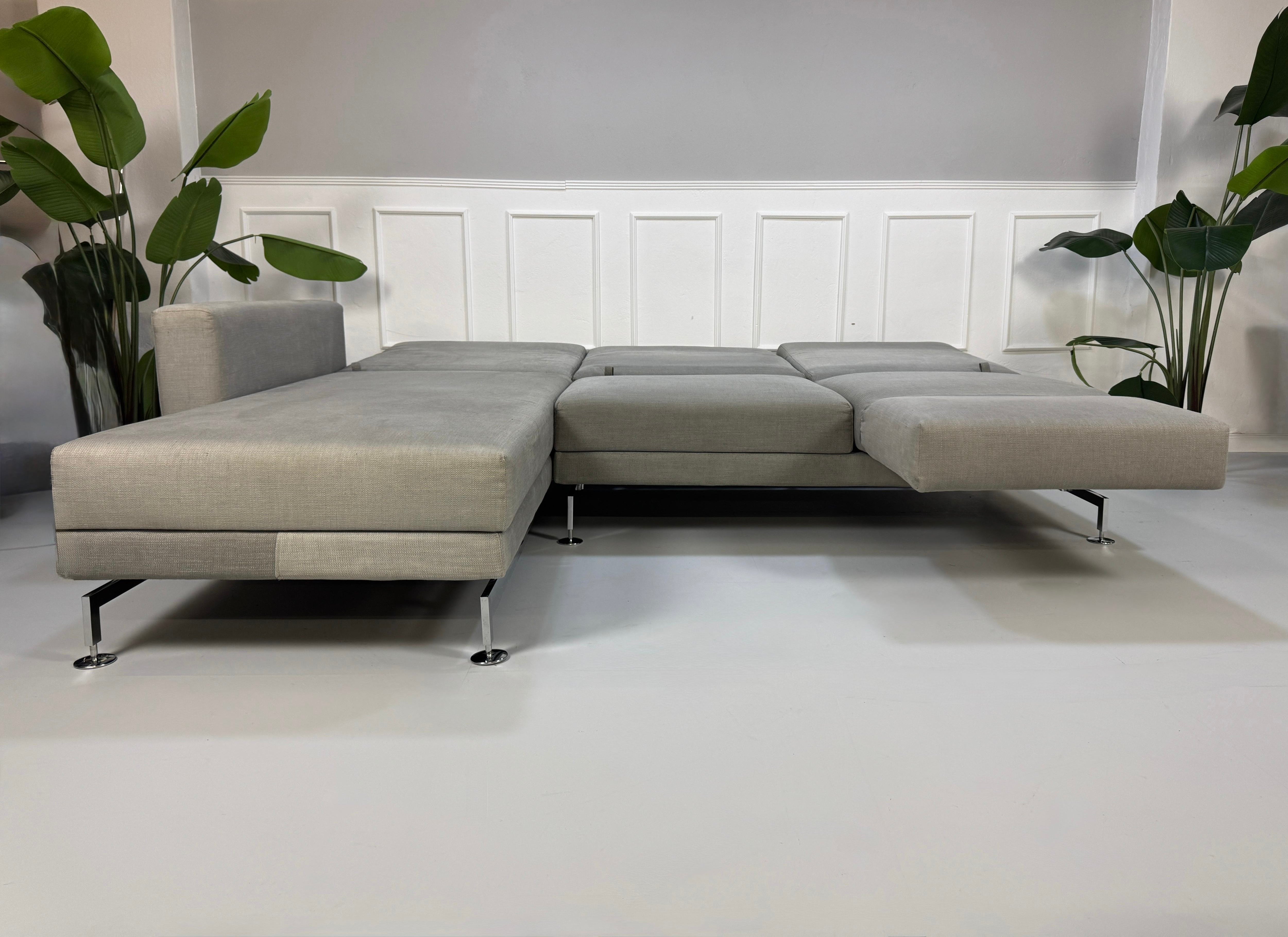 Gebrauchtes graues Brühl Moule Designer Stoff Sofa vor einer Wand, stilvoll und modern eingerichtet.