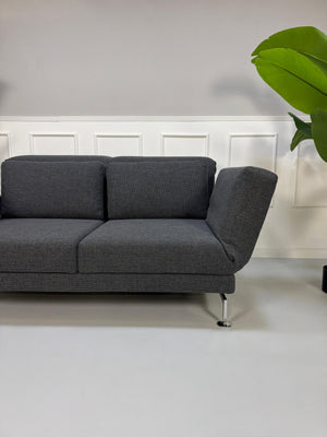 Graues Ausstellungsstück Brühl Moule Designer Stoff Sofa vor einer Wand, stilvoll und modern eingerichtet.