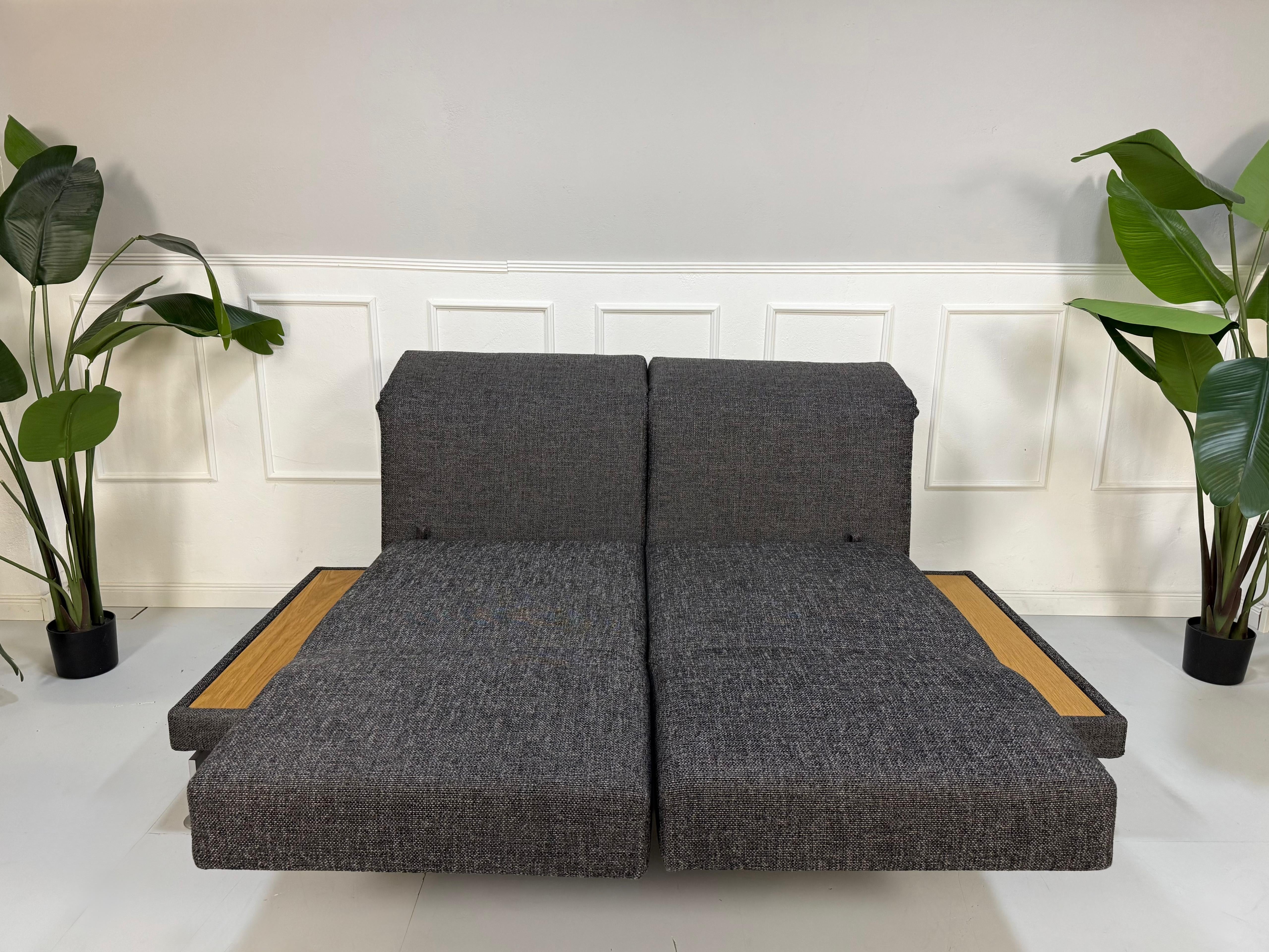 Ausstellungsstück Brühl Moule Designer Stoff Sofa in Grau vor einer Wand, stilvoll und modern eingerichtet.