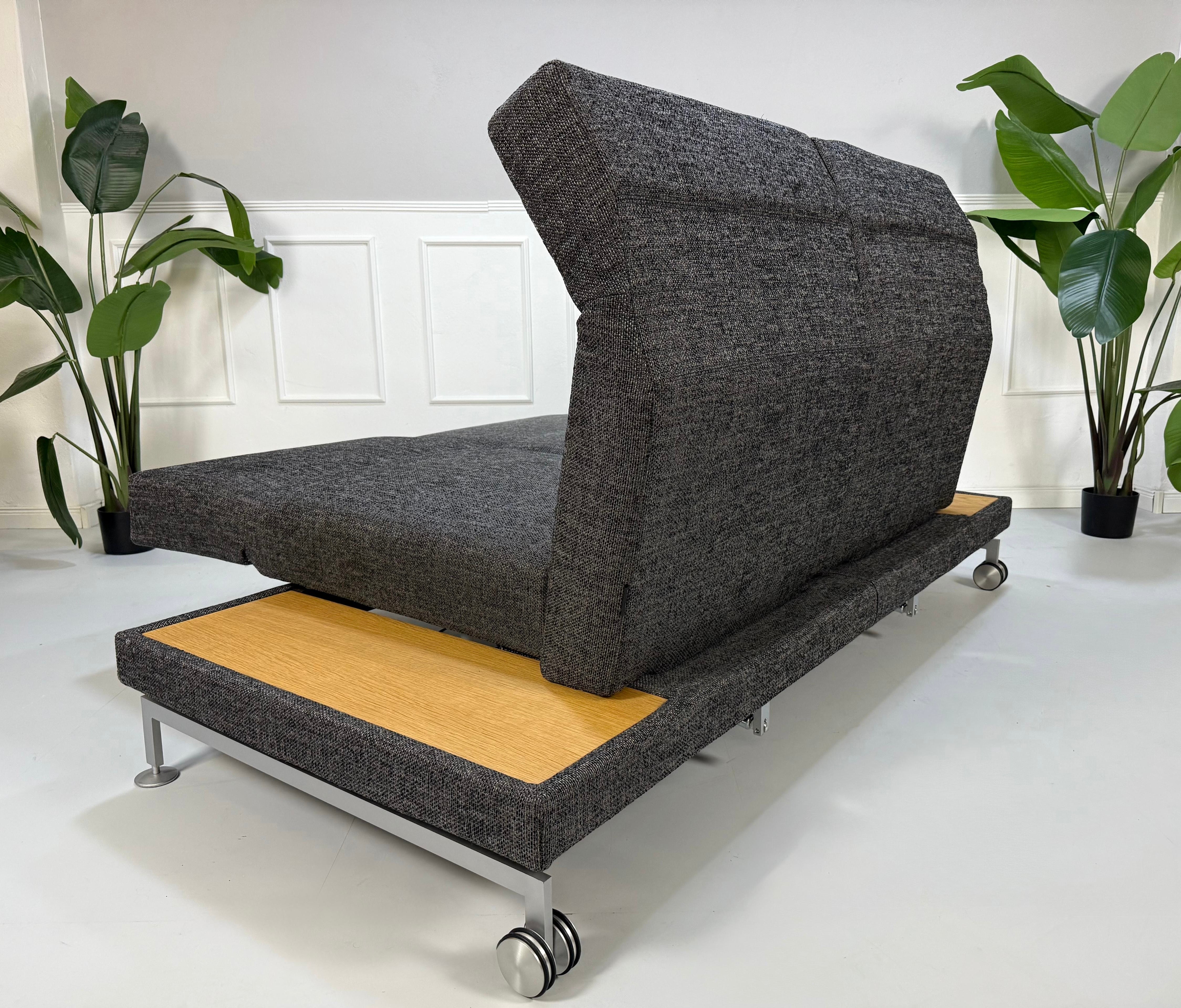 Ausstellungsstück Brühl Moule Designer Stoff Sofa in Grau vor einer Wand, stilvoll und modern eingerichtet.