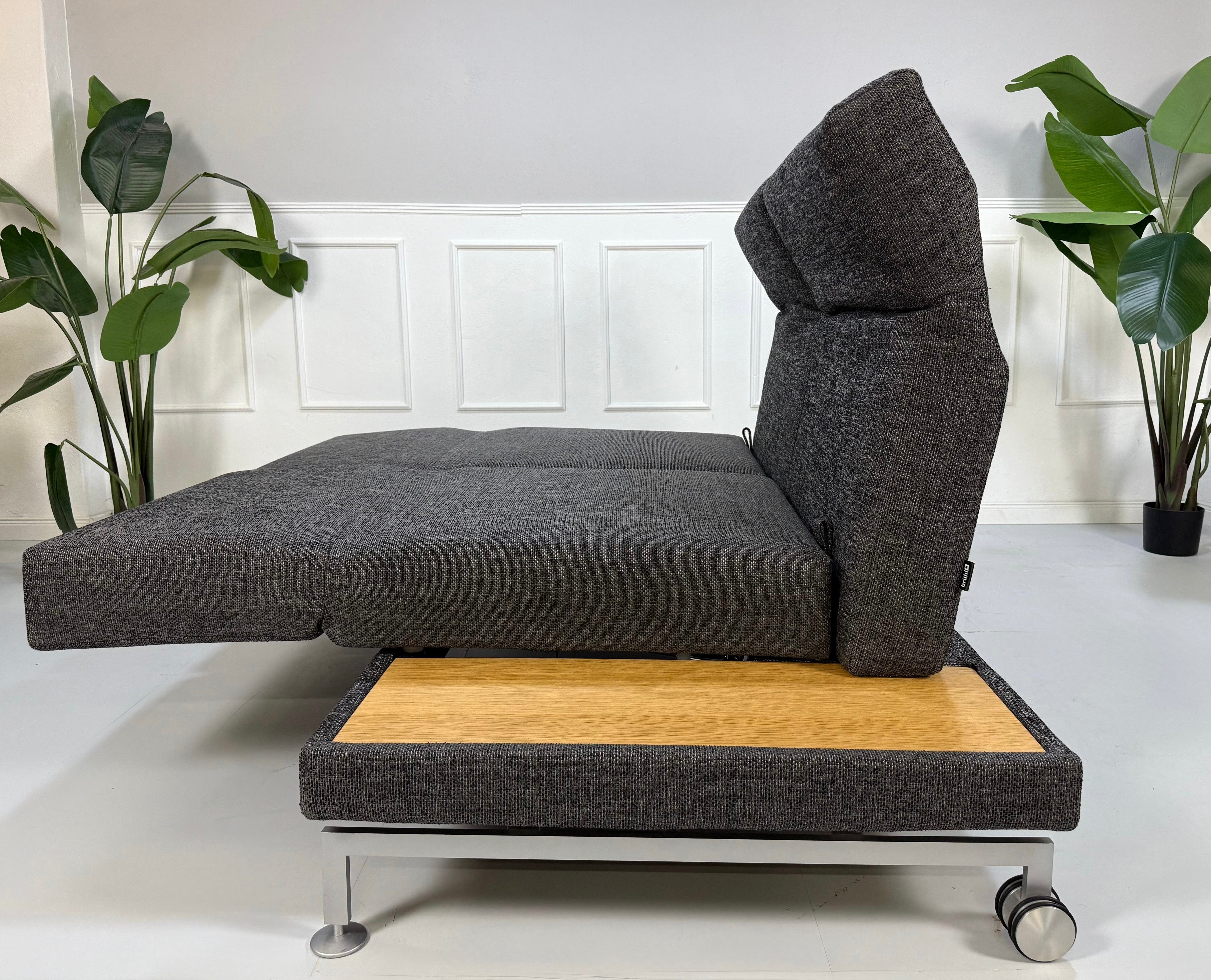 Ausstellungsstück Brühl Moule Designer Stoff Sofa in Grau vor einer Wand, stilvoll und modern eingerichtet.